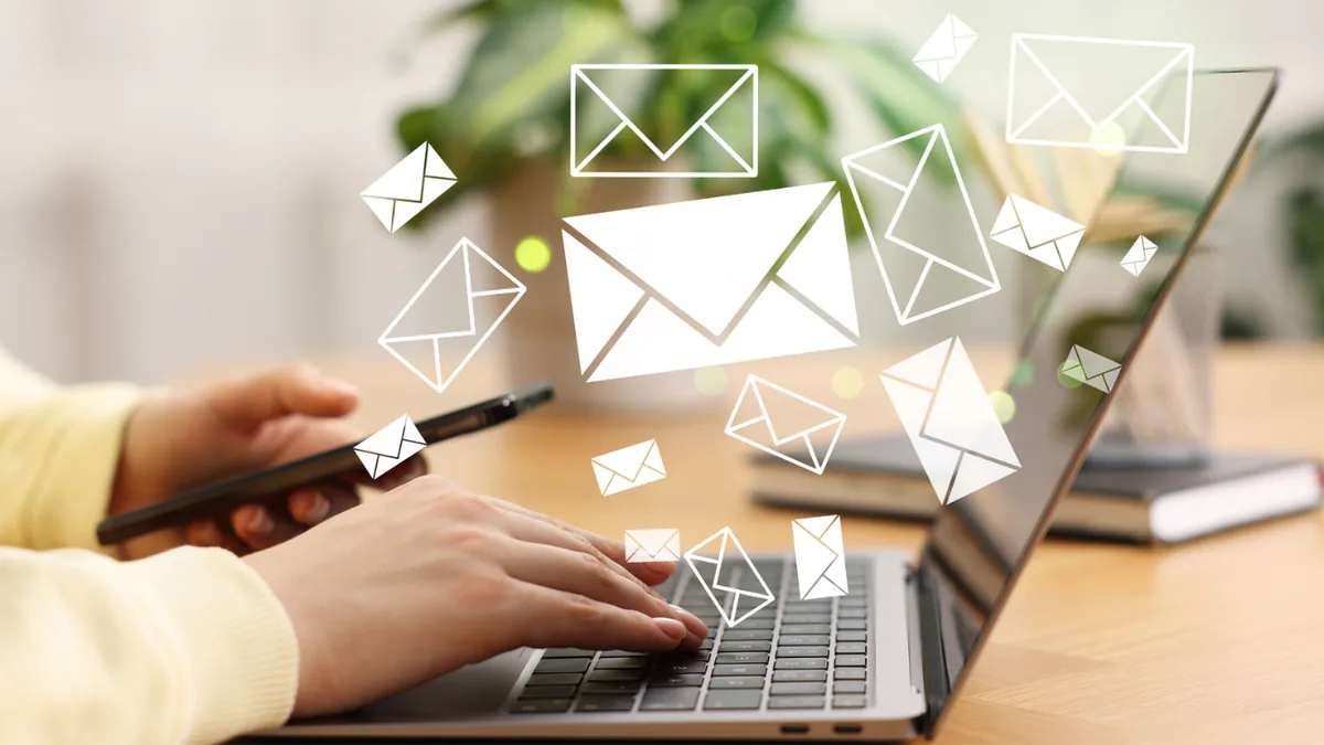 Person typing on a laptop with email envelope icons floating above the keyboard